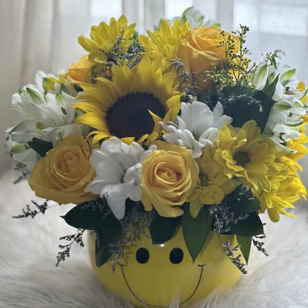 Yellow and white flower arrangement in a smiley-face container