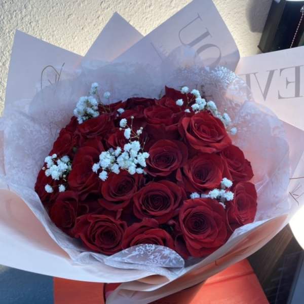 Hand-tied bouquet of red roses with white filler flowers wrapped in soft pink paper