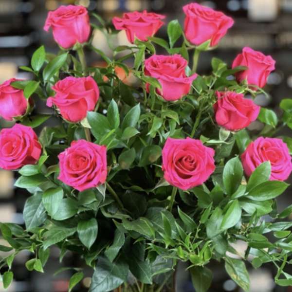 Tall arrangement of bright pink roses with lush greenery in a clear glass vase