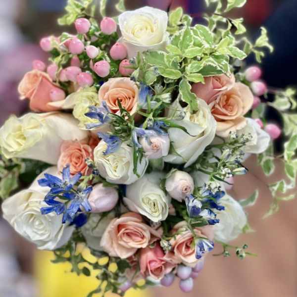 Bouquet of white, blush, and peach roses with blue flowers and pink berries