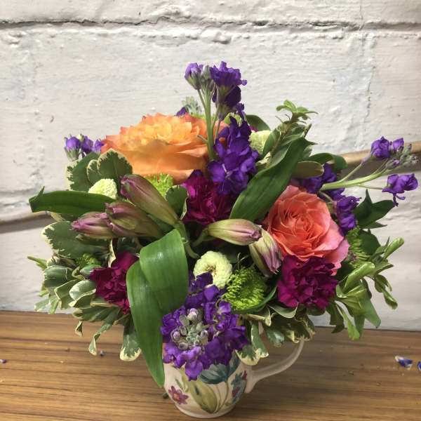 Colorful bouquet of orange and purple flowers in a floral ceramic pitcher