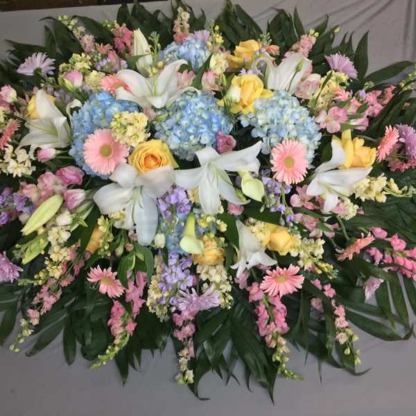 Large pastel floral spray with lilies, hydrangeas, and daisies on dark foliage