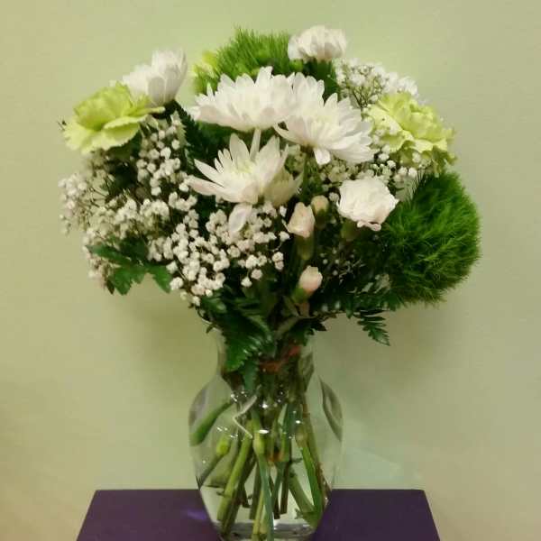 White flowers and green carnations arranged in a clear glass vase