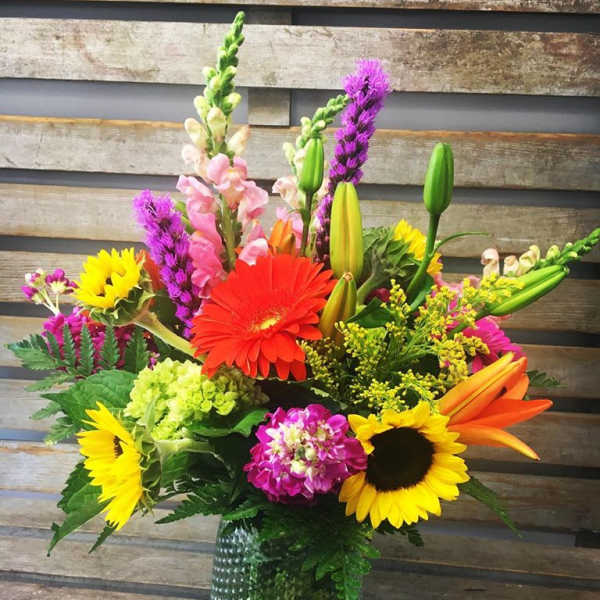 Colorful mixed bouquet in a green glass vase with sunflowers and lilies
