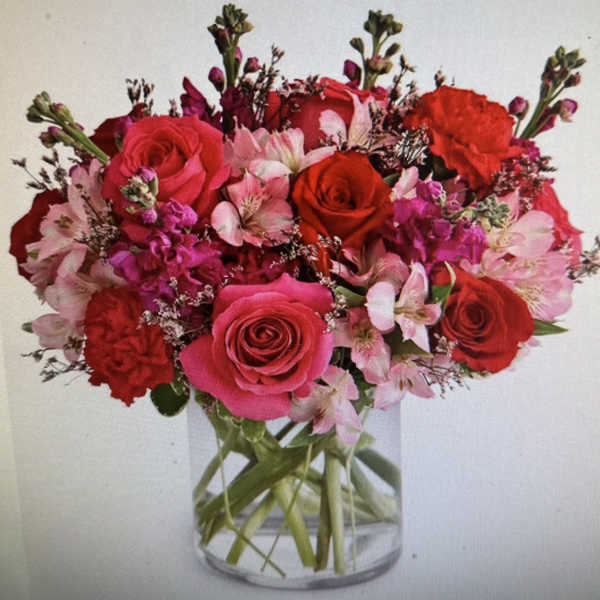 Round arrangement of red and pink roses, carnations, and alstroemeria in a clear glass vase
