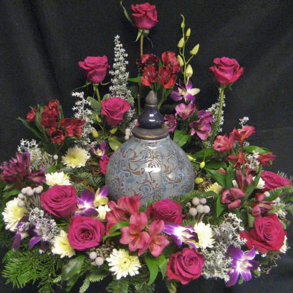 Floral arrangement with pink roses and mixed blooms around a decorative urn