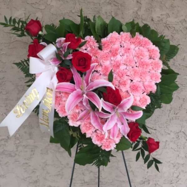 Heart-shaped floral spray with pink carnations, red roses, and lilies on an easel