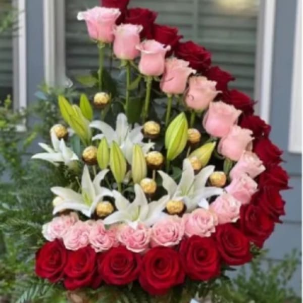 Heart-shaped floral arrangement with red and pink roses and white lilies in a basket