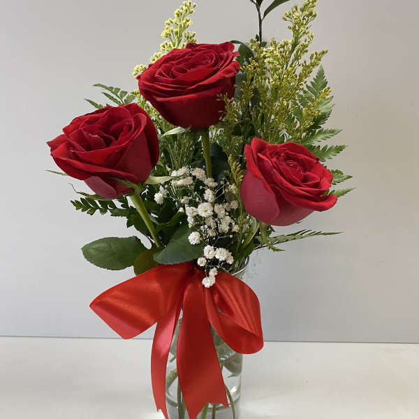 Three red roses in a clear glass vase with a red ribbon