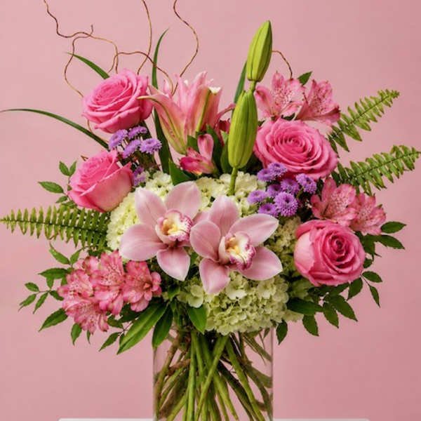 Pink roses, lilies, and orchids arranged in a clear glass vase