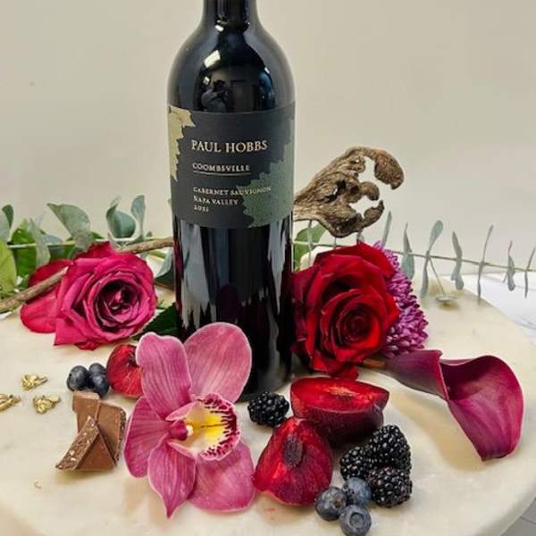 Wine bottle surrounded by roses, orchid petals, and berries