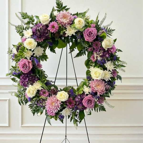 Floral wreath on a black stand with pink, white, and purple blooms