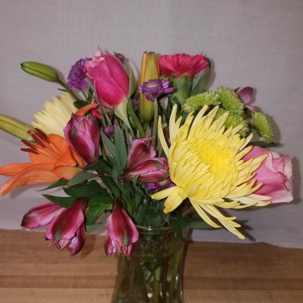 Mixed bouquet of pink, yellow, orange, and purple flowers in a glass vase