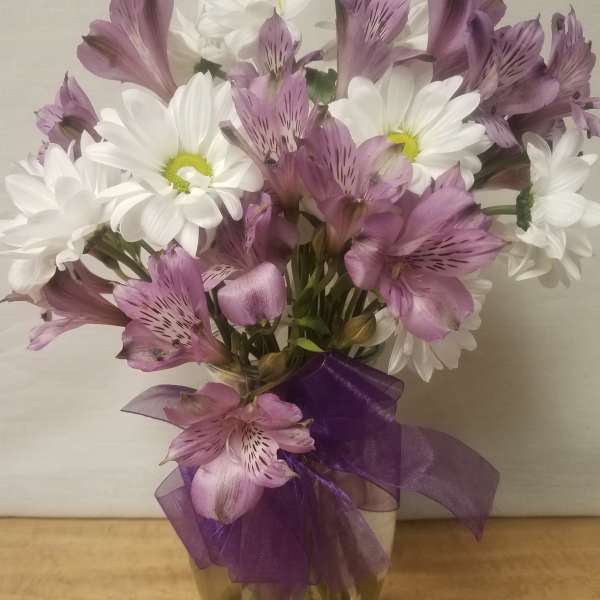 White daisies and purple alstroemeria in a glass vase with a purple ribbon