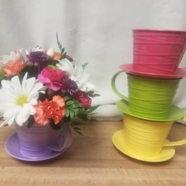 Colorful bouquet in a purple teacup-shaped container beside stacked teacup planters