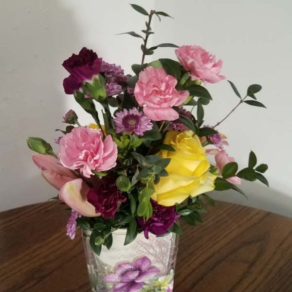 Mixed pink, purple, and yellow flowers in a clear square vase