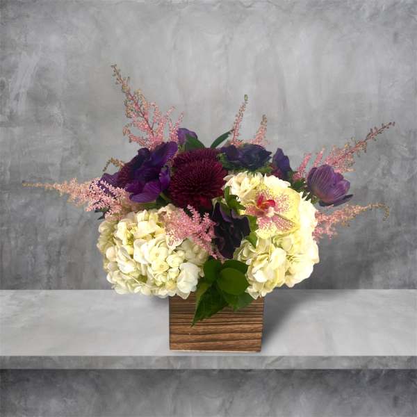 Purple and cream floral arrangement in a wooden square vase