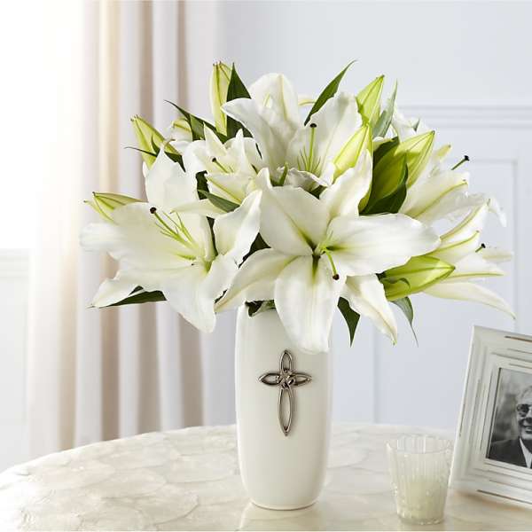 White lilies arranged in a tall white vase with a cross emblem