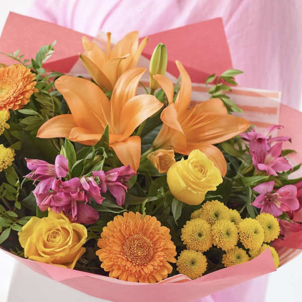 Bouquet of orange lilies, yellow roses, and pink alstroemeria in pink wrap