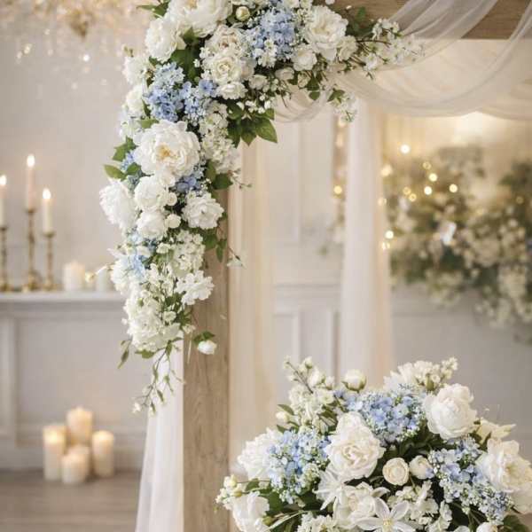 White and pale blue floral wedding arrangements on a draped arch and low pedestal