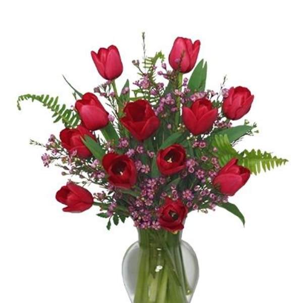 Red tulips and small pink flowers arranged in a clear glass vase