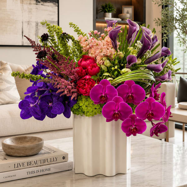 Large arrangement of purple orchids, calla lilies, and pink flowers in a white vase