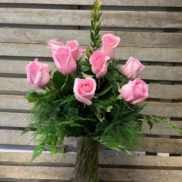 Pink roses arranged in a clear glass vase with lush greenery