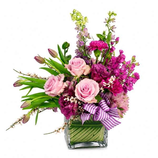 Pink roses and magenta flowers in a square glass vase with a striped ribbon