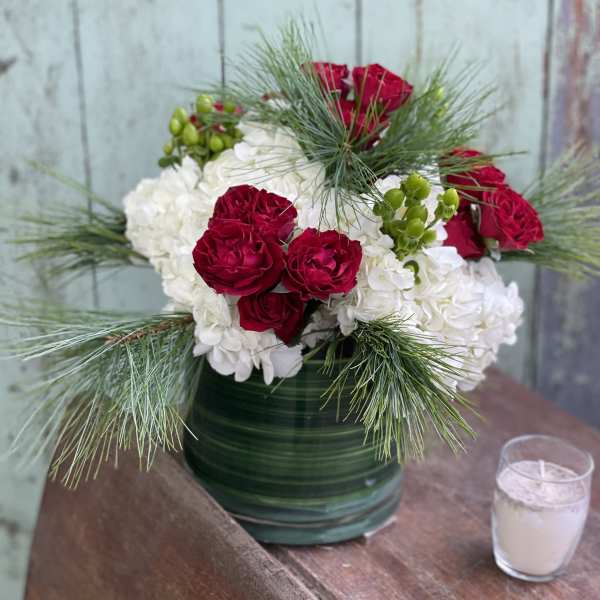 Red roses and white hydrangeas in a green vase with pine accents