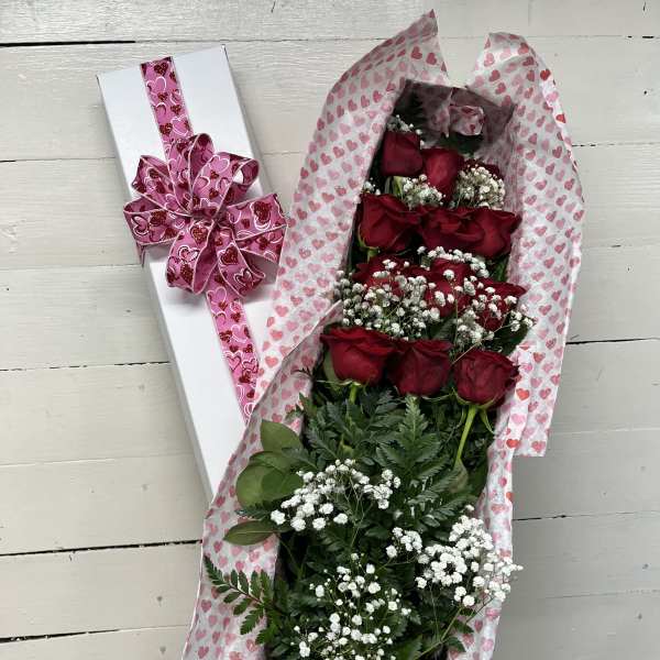 Bouquet of red roses in heart-patterned wrap beside a white gift box with pink ribbon