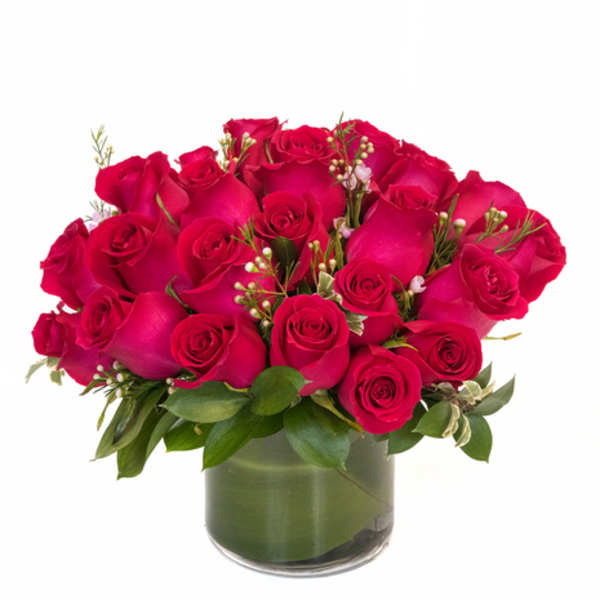 Compact arrangement of hot pink roses in a low clear glass cylinder vase with a leaf-wrapped base