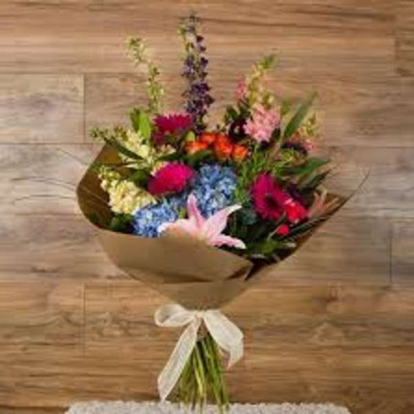 Mixed bouquet of colorful flowers wrapped in brown paper with a white ribbon