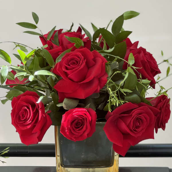 Red roses arranged in a square glass vase with greenery