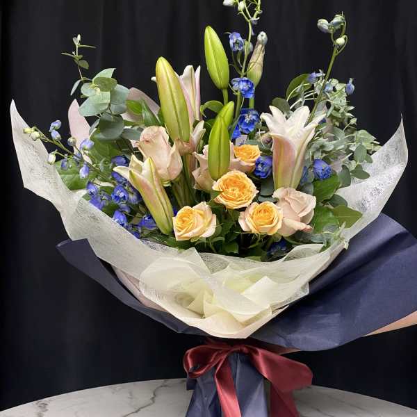 Bouquet of lilies, roses, and blue flowers wrapped in navy paper