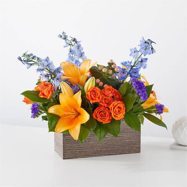 Orange roses and yellow lilies in a rectangular wooden box with blue flowers