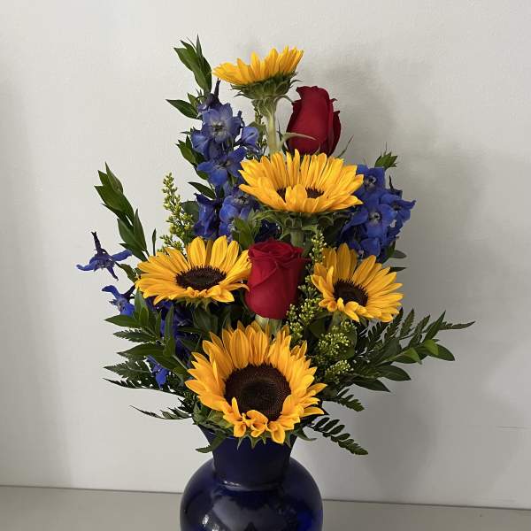 Sunflowers, red roses, and blue flowers arranged in a dark blue vase