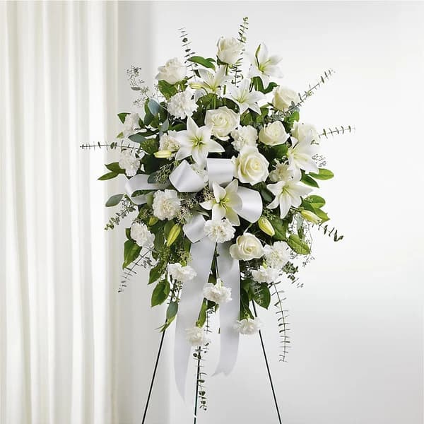 White floral standing spray with lilies, roses, and ribbon on an easel