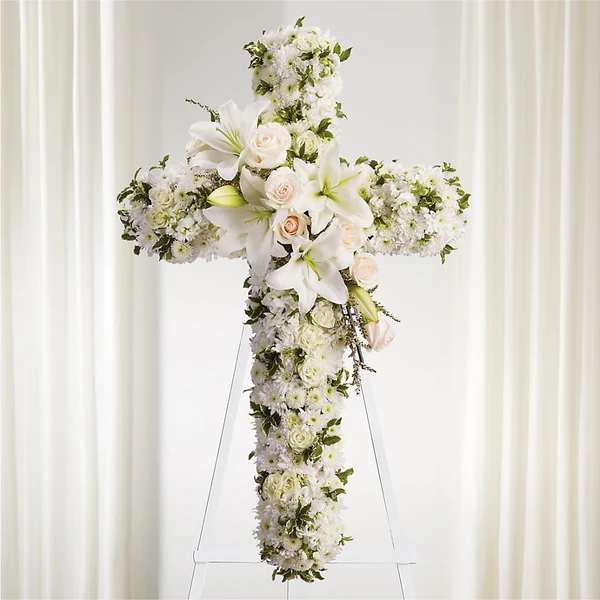 White floral cross arrangement with roses and lilies on a stand