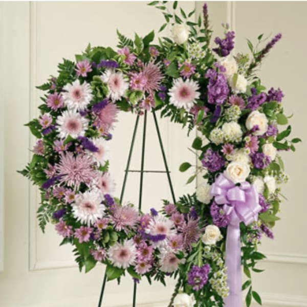Purple and white floral wreath on a stand with a lavender ribbon
