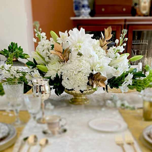 White floral centerpiece in a gold bowl on a dining table