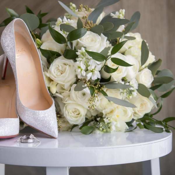 White rose bouquet with silver high heels and wedding rings on a table