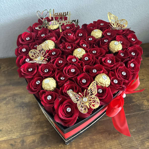 Heart-shaped box of red roses with chocolates and a Happy Anniversary topper