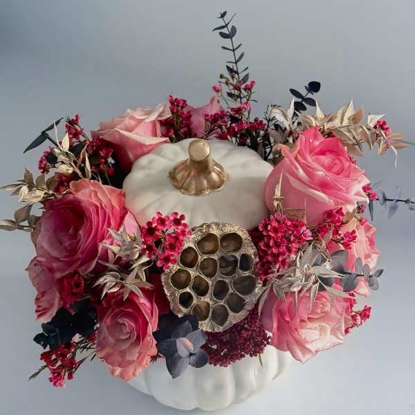 Pink roses arranged around a white pumpkin centerpiece