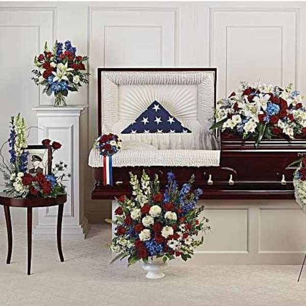 Funeral casket surrounded by patriotic red, white, and blue floral sprays