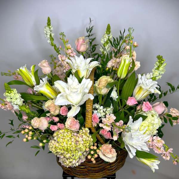 Basket arrangement of white lilies, pink roses, and pale blooms