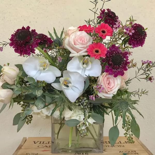 Mixed bouquet with pink roses, white orchids, and magenta blooms in a glass vase