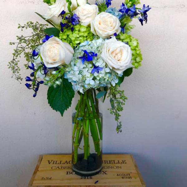 White roses and blue flowers arranged in a tall glass vase