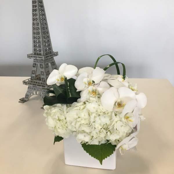 White orchids and hydrangeas in a white box beside a small Eiffel Tower decoration