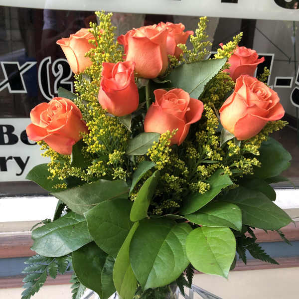 Orange roses in a clear glass vase with yellow filler flowers