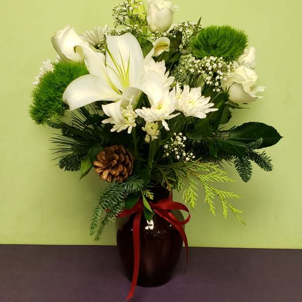 White lilies and roses arranged in a dark vase with a red ribbon